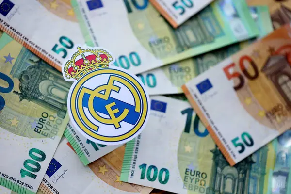 KYIV, UKRAINE - 23 Şubat 2025 Real Madrid CF futbol kulübü rozeti büyük miktarda EURO para banknotlarının üzerinde yatıyor