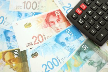 Israel New Shekels banknotları ve hesap makinesi. Mevcut İsrail para faturaları ve kalibreleri büyük miktarda masada yatıyor. İsrail 'de vergilendirme ve para kavramı