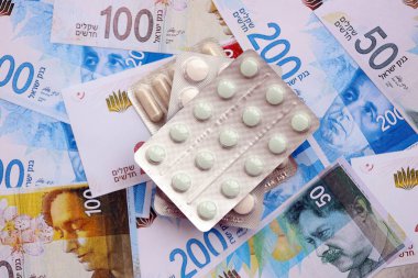 Israel New Shekels banknotları ve ilaç hapları. Mevcut İsrail para ve uyuşturucu faturaları büyük miktarda masada yatıyor. İsrail 'de ilaç ve eczane kavramı