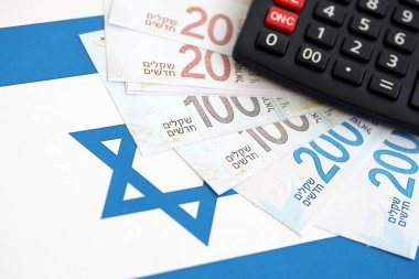 Israel New Shekels banknotları ve hesap makinesi bayrağın üzerinde. İsrail 'in mevcut para faturaları ve kalibreleri büyük oranda bayrakta yatıyor. İsrail 'de vergilendirme ve para kavramı