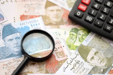 Pakistan banknotları ve büyüteçle hesap makinesi. Mevcut Pakistan para faturaları ve loupe ile calc büyük miktarda masada yatıyor. Pakistan 'da vergi ve para sayımı kavramı