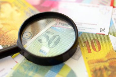 İsviçre frangı banknotları ve büyüteç. İçinde loupe olan şu anki para banknotları büyük miktarda masada yatıyor. İsviçre 'de mali izleme ve vergilendirme kavramı
