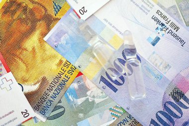 İsviçre frangı banknotları ve ilaç şişeleri. Mevcut para faturaları ve enjeksiyon dozu büyük miktarda masada yatıyor. İsviçre 'de ilaç ve aşı kavramı