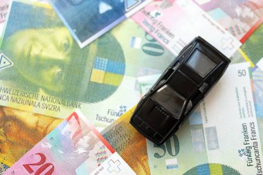 İsviçre frangı banknotları ve oyuncak araba. Mevcut frank, faturalar ve siyah araba büyük miktarda masada yatıyor. İsviçre 'de araba sahibi olma kavramı