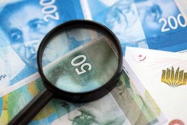 Israel New Shekels banknotları ve büyüteç. Şu anki İsrail 'in yüksek meblağlı faturaları masanın üzerinde yatıyor. İsrail 'de mali izleme ve vergilendirme kavramı