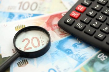 Israel New Shekels banknotları ve büyüteçle birlikte hesap makinesi. Mevcut İsrail para faturaları ve loupe ile calc büyük miktarda masada yatıyor. İsrail 'de vergilendirme ve para kavramı
