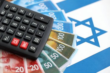 Israel New Shekels banknotları ve hesap makinesi bayrağın üzerinde. İsrail 'in mevcut para faturaları ve kalibreleri büyük oranda bayrakta yatıyor. İsrail 'de vergilendirme ve para kavramı