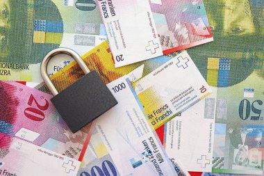 İsviçre frangı banknotları ve asma kilit. Mevcut para banknotları büyük miktarda masada yatıyor. İsviçre 'de yaptırımlar ve mali güvenlik kavramı
