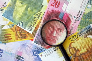 İsviçre frangı banknotları ve büyüteç. İçinde loupe olan şu anki para banknotları büyük miktarda masada yatıyor. İsviçre 'de mali izleme ve vergilendirme kavramı