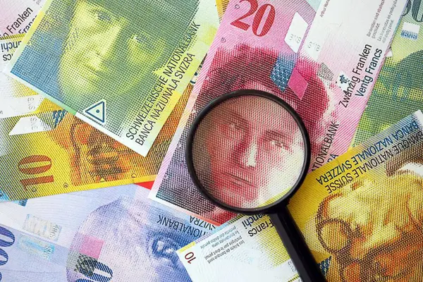 İsviçre frangı banknotları ve büyüteç. İçinde loupe olan şu anki para banknotları büyük miktarda masada yatıyor. İsviçre 'de mali izleme ve vergilendirme kavramı