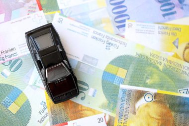 İsviçre frangı banknotları ve oyuncak araba. Mevcut frank, faturalar ve siyah araba büyük miktarda masada yatıyor. İsviçre 'de araba sahibi olma kavramı