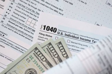 Yüz dolarlık banknotlar ve 1040 bireysel gelir vergisi iade formu yakın çekim. Çok az Amerikan doları ve Birleşik Devletler vergisi yok. ABD 'de vergi ödeme ve muhasebe kavramı