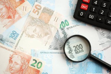 Brezilya reais banknotları ve büyüteçli hesap makinesi. Mevcut Brezilya gerçek para faturaları ve loupe ile calc büyük miktarda masada yatıyor. Brezilya 'da vergilendirme ve para konsepti