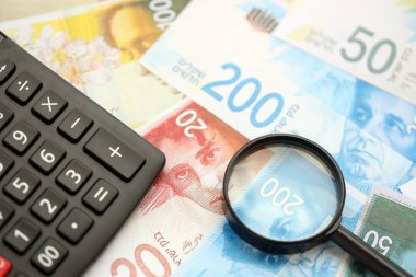 Israel New Shekels banknotları ve büyüteçle birlikte hesap makinesi. Mevcut İsrail para faturaları ve loupe ile calc büyük miktarda masada yatıyor. İsrail 'de vergilendirme ve para kavramı