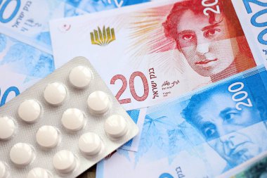 Israel New Shekels banknotları ve ilaç hapları. Mevcut İsrail para ve uyuşturucu faturaları büyük miktarda masada yatıyor. İsrail 'de ilaç ve eczane kavramı