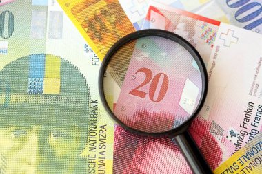 İsviçre frangı banknotları ve büyüteç. İçinde loupe olan şu anki para banknotları büyük miktarda masada yatıyor. İsviçre 'de mali izleme ve vergilendirme kavramı