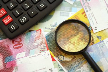 İsviçre frangı banknotları ve büyüteçli hesap makinesi. Mevcut para faturaları ve loupe ile calc büyük miktarda masada yatıyor. İsviçre 'de vergilendirme ve iş kavramı