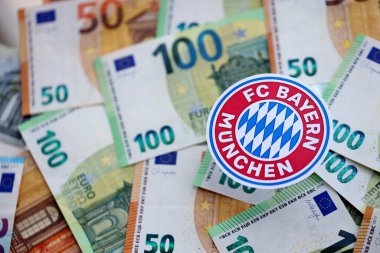 KYIV, UKRAINE - 23 Şubat 2025 Bayern Münih futbol kulübü rozeti büyük miktarda EURO para banknotları üzerinde yatıyor