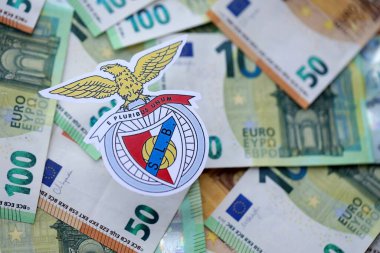 KYIV, UKRAINE - 23 Şubat 2025 Sport Lisboa ve Benfica futbol kulübü rozeti büyük miktarda EURO para banknotlarının üzerinde yatıyor
