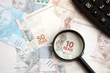 Brezilya reais banknotları ve büyüteçli hesap makinesi. Mevcut Brezilya gerçek para faturaları ve loupe ile calc büyük miktarda masada yatıyor. Brezilya 'da vergilendirme ve para konsepti