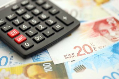 Israel New Shekels banknotları ve hesap makinesi. Mevcut İsrail para faturaları ve kalibreleri büyük miktarda masada yatıyor. İsrail 'de vergilendirme ve para kavramı