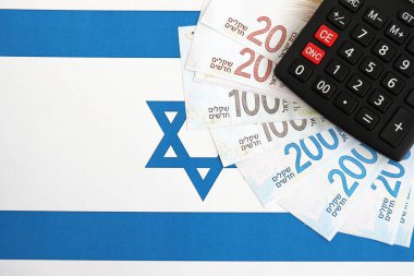 Israel New Shekels banknotları ve hesap makinesi bayrağın üzerinde. İsrail 'in mevcut para faturaları ve kalibreleri büyük oranda bayrakta yatıyor. İsrail 'de vergilendirme ve para kavramı