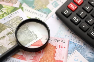 Pakistan banknotları ve büyüteçle hesap makinesi. Mevcut Pakistan para faturaları ve loupe ile calc büyük miktarda masada yatıyor. Pakistan 'da vergi ve para sayımı kavramı