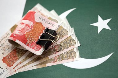 Pakistan bayrağı üzerinde Pakistan banknotları. Pakistan 'ın mevcut para faturaları büyük miktarlarda pankartta yatıyor. Pakistan 'da ekonomi ve ticaret kavramı