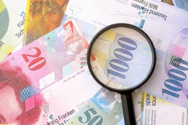 İsviçre frangı banknotları ve büyüteç. İçinde loupe olan şu anki para banknotları büyük miktarda masada yatıyor. İsviçre 'de mali izleme ve vergilendirme kavramı