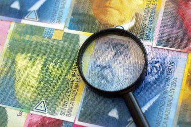 İsviçre frangı banknotları ve büyüteç. Loupe 'un para faturaları büyük miktarda masada duruyor. İsviçre 'de mali izleme ve vergilendirme kavramı