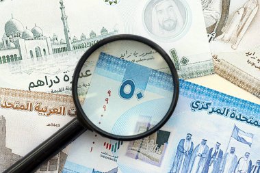 Birleşik Arap Emirlikleri kara para birimi banknotları ve büyüteç yakın çekim. Finansal izleme ve vergilendirme kavramı