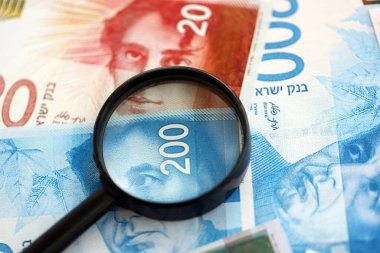 Israel New Shekels banknotları ve büyüteç. Şu anki İsrail 'in yüksek meblağlı faturaları masanın üzerinde yatıyor. İsrail 'de mali izleme ve vergilendirme kavramı