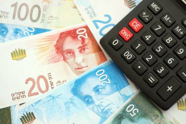 Israel New Shekels banknotları ve hesap makinesi. Mevcut İsrail para faturaları ve kalibreleri büyük miktarda masada yatıyor. İsrail 'de vergilendirme ve para kavramı