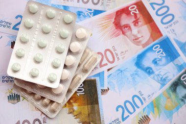 Israel New Shekels banknotları ve ilaç hapları. Mevcut İsrail para ve uyuşturucu faturaları büyük miktarda masada yatıyor. İsrail 'de ilaç ve eczane kavramı