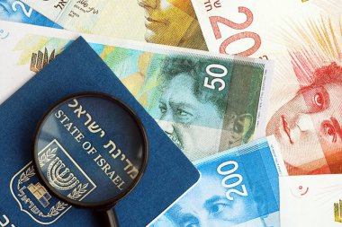 Israel New Shekels banknotları ve Louise 'li pasaport. İsrail 'in mevcut para faturaları ve biyometrik geçiş kartı büyük miktarda masada yatıyor. İsrail 'de seyahat ve tatil kavramı