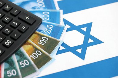 Israel New Shekels banknotları ve hesap makinesi bayrağın üzerinde. İsrail 'in mevcut para faturaları ve kalibreleri büyük oranda bayrakta yatıyor. İsrail 'de vergilendirme ve para kavramı
