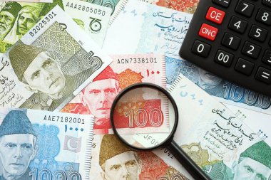 Pakistan banknotları ve büyüteçle hesap makinesi. Mevcut Pakistan para faturaları ve loupe ile calc büyük miktarda masada yatıyor. Pakistan 'da vergi ve para sayımı kavramı