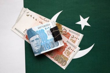 Pakistan bayrağı üzerinde Pakistan banknotları. Pakistan 'ın mevcut para faturaları büyük miktarlarda pankartta yatıyor. Pakistan 'da ekonomi ve ticaret kavramı