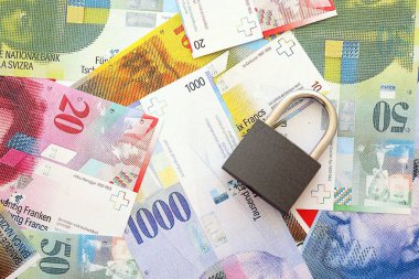 İsviçre frangı banknotları ve asma kilit. Mevcut para banknotları büyük miktarda masada yatıyor. İsviçre 'de yaptırımlar ve mali güvenlik kavramı