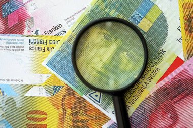 İsviçre frangı banknotları ve büyüteç. İçinde loupe olan şu anki para banknotları büyük miktarda masada yatıyor. İsviçre 'de mali izleme ve vergilendirme kavramı