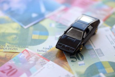 İsviçre frangı banknotları ve oyuncak araba. Mevcut frank, faturalar ve siyah araba büyük miktarda masada yatıyor. İsviçre 'de araba sahibi olma kavramı