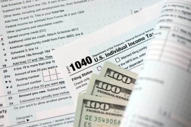 Yüz dolarlık banknotlar ve 1040 bireysel gelir vergisi iade formu yakın çekim. Çok az Amerikan doları ve Birleşik Devletler vergisi yok. ABD 'de vergi ödeme ve muhasebe kavramı