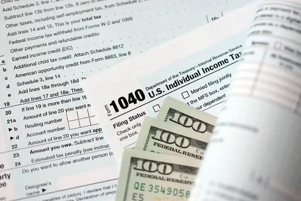 Yüz dolarlık banknotlar ve 1040 bireysel gelir vergisi iade formu yakın çekim. Çok az Amerikan doları ve Birleşik Devletler vergisi yok. ABD 'de vergi ödeme ve muhasebe kavramı