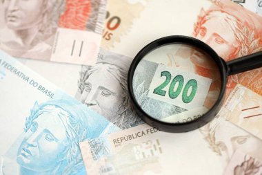 Brezilya reais banknotları ve büyüteç. Mevcut Brezilya gerçek para faturaları ve loupe büyük miktarda masada yatıyor. Brezilya 'da mali izleme ve vergilendirme kavramı