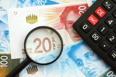 Israel New Shekels banknotları ve büyüteçle birlikte hesap makinesi. Mevcut İsrail para faturaları ve loupe ile calc büyük miktarda masada yatıyor. İsrail 'de vergilendirme ve para kavramı