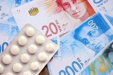 Israel New Shekels banknotları ve ilaç hapları. Mevcut İsrail para ve uyuşturucu faturaları büyük miktarda masada yatıyor. İsrail 'de ilaç ve eczane kavramı