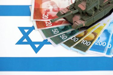 Israel New Shekels 'ın banknotları ve oyuncak tankları bayrağın üzerinde. İsrail 'in şu anki para ve tankı büyük oranda bayraklar üzerinde duruyor. İsrail 'de ordu fonları ve silah satışları kavramı