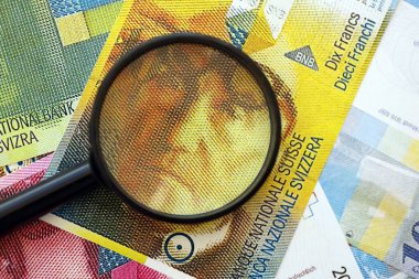 İsviçre frangı banknotları ve büyüteç. İçinde loupe olan şu anki para banknotları büyük miktarda masada yatıyor. İsviçre 'de mali izleme ve vergilendirme kavramı