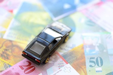 İsviçre frangı banknotları ve oyuncak araba. Mevcut frank, faturalar ve siyah araba büyük miktarda masada yatıyor. İsviçre 'de araba sahibi olma kavramı
