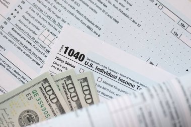 Yüz dolarlık banknotlar ve 1040 bireysel gelir vergisi iade formu yakın çekim. Çok az Amerikan doları ve Birleşik Devletler vergisi yok. ABD 'de vergi ödeme ve muhasebe kavramı